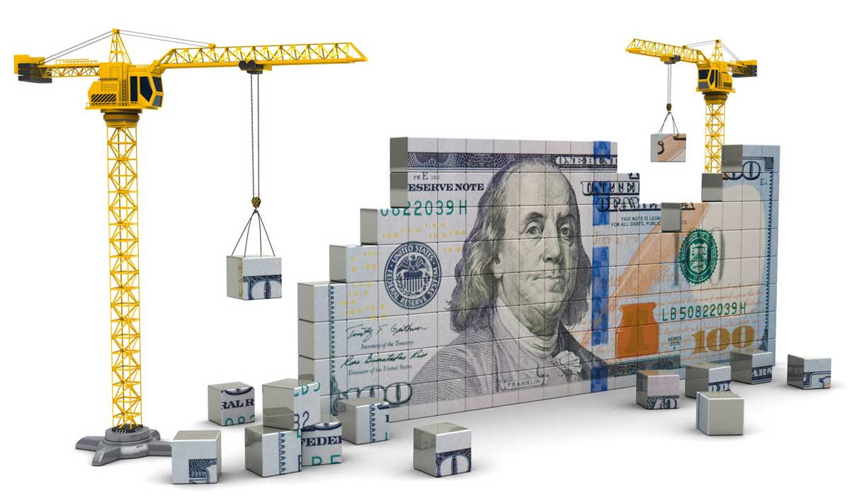 A wall that resembles a 100 dollar bill being build by cranes