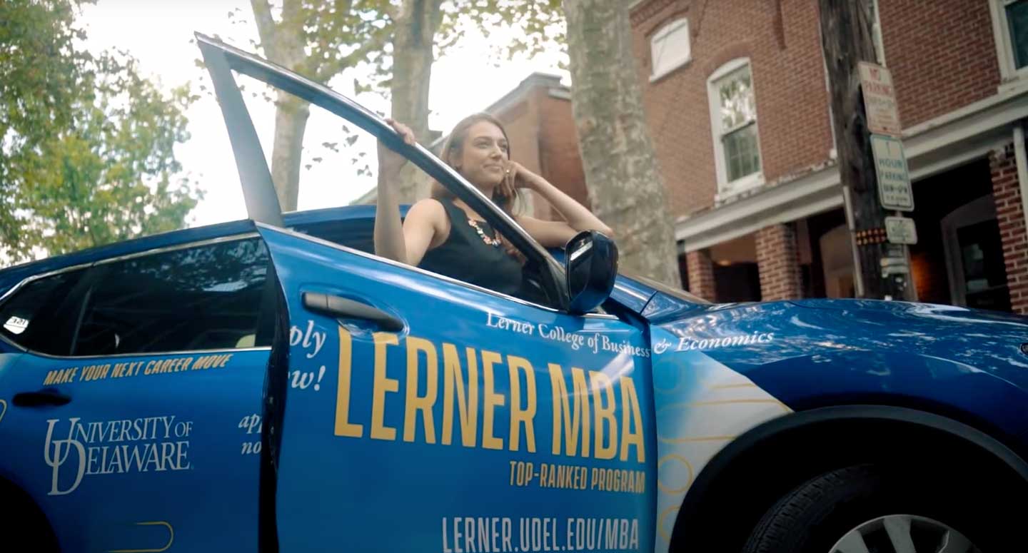 Woman standing next to car wrapped in advertisement for University of Delaware