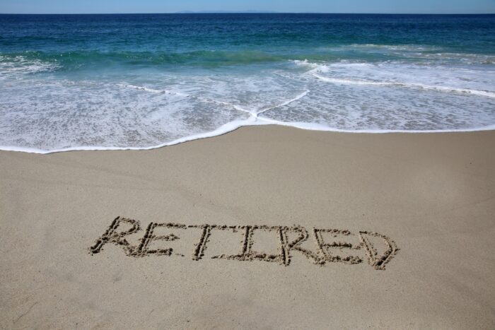 Retirement written in sand on a beach by blue ocean water