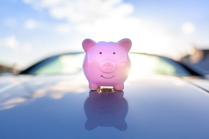 Piggy bank sits on the hood of the car with a sunset on the background