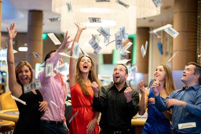 Group of friends at the casino celebrating a big win throwing money to the air all looking very happy