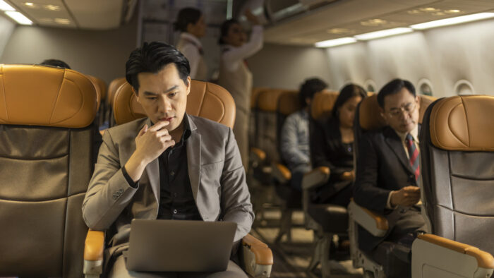 Young business man using computer notebook to connect and check his work in an airplane cabin before boarding. Traveler enjoys internet connection while taking a flight