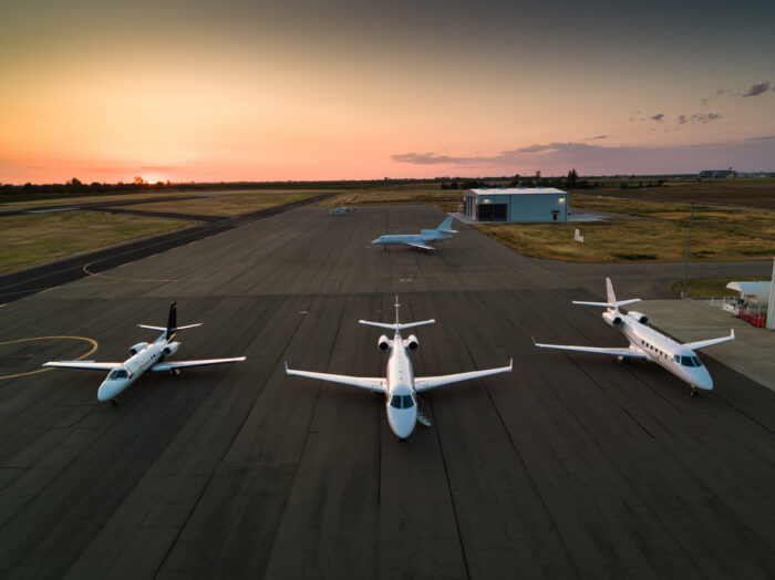 Four private jets parked on the runway, shot at sunset.
