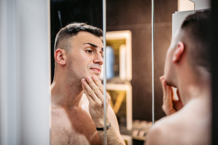 Handsome young man looking at himself in the bathroom mirror.