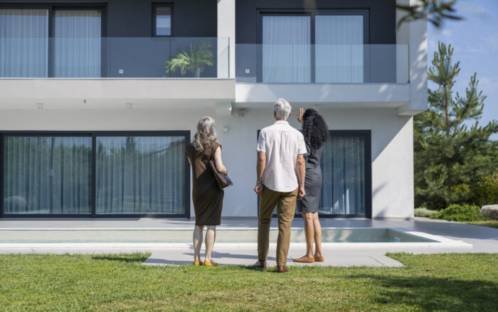 Female real estate agent talking to senior couple standing by swimming pool while showing new luxury house on sunny day. Luxury lifestyles and new beginning concept.