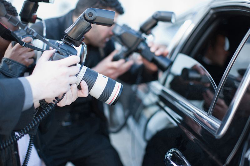 Three Paparazzi Members with Cameras Taking Photos of Someone Inside a the Back Seat of a Black Car with the Window Down, Left Side of the Car