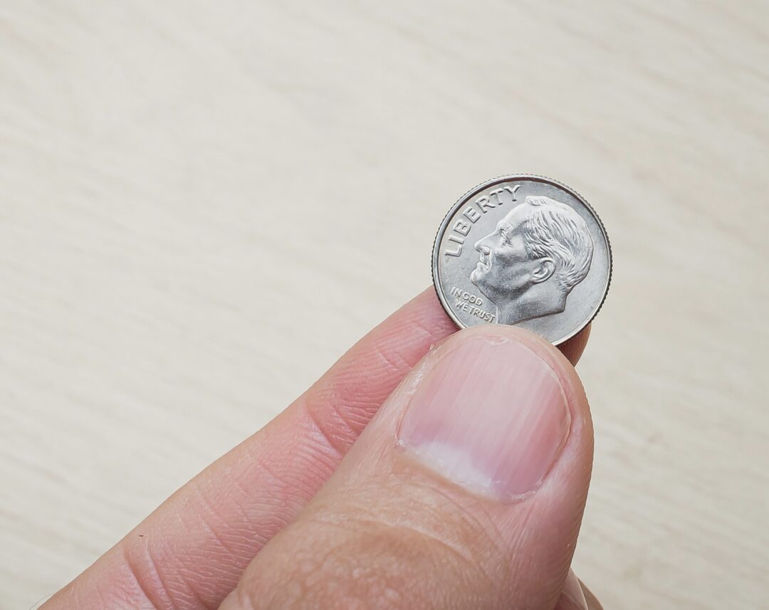 Photograph of a man holding an american dollar dime.