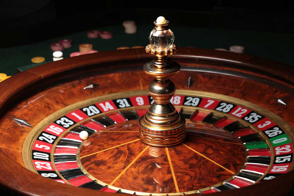 A close-up of a roulette wheel with a white ball resting on the number 13 black. Casino chips are scattered in the blurred background.