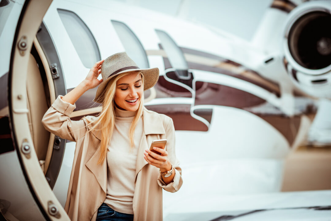 Young successful girl getting out of a private jet parked on a runway. She is using a mobile phone.