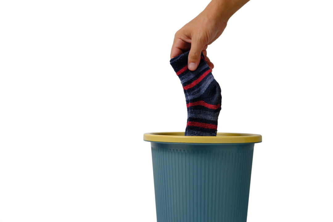 Man hand throws an old sock into trash on white background of isolate