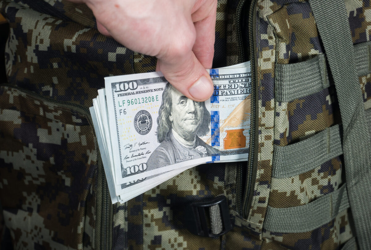 Man is putting in a military backpack dollars."nDark green Camouflage khaki bag with money.