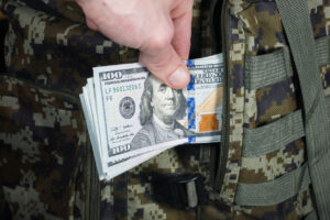 Man is putting in a military backpack dollars."nDark green Camouflage khaki bag with money.