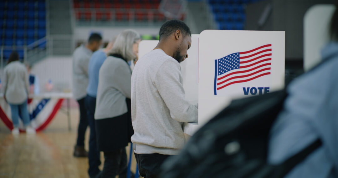 Elderly male voter with bulletin in hands comes to voting booth. Multicultural American citizens come to vote in polling station. Political races of US presidential candidates. National Election Day.