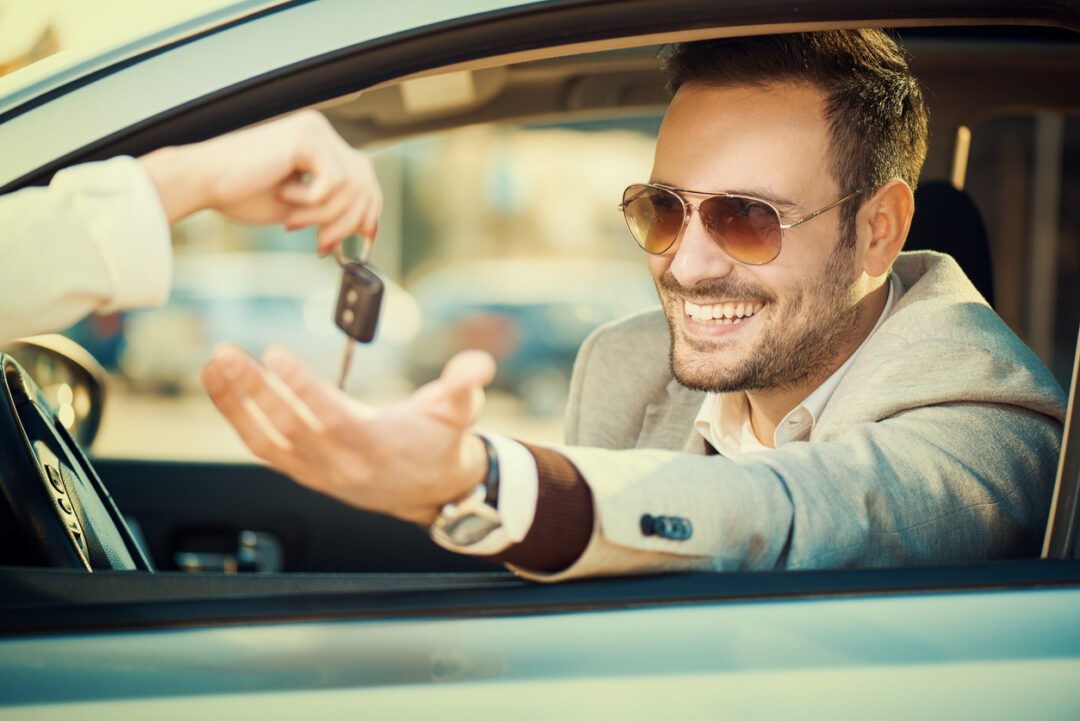 Handsome men sitting in a car at car dealership.He is receiving key from his new car.