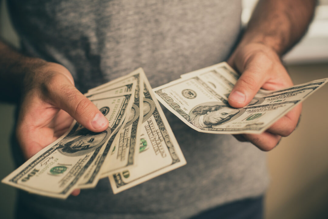 A man in a gray T-shirt holds dollars in his hands. Bank. Casino. Salary. Rates.