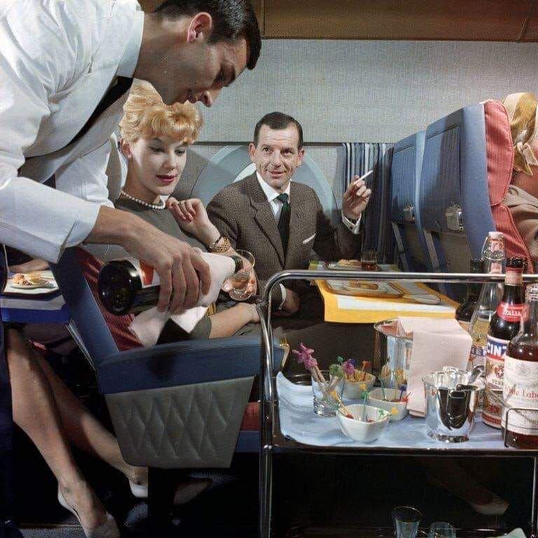 First class passengers getting served champagne on a flight in the 60s