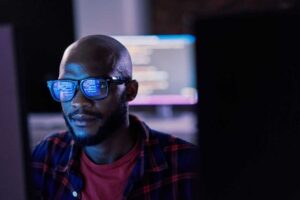 Man sitting in front of a computer screen with code reflected in his glasses