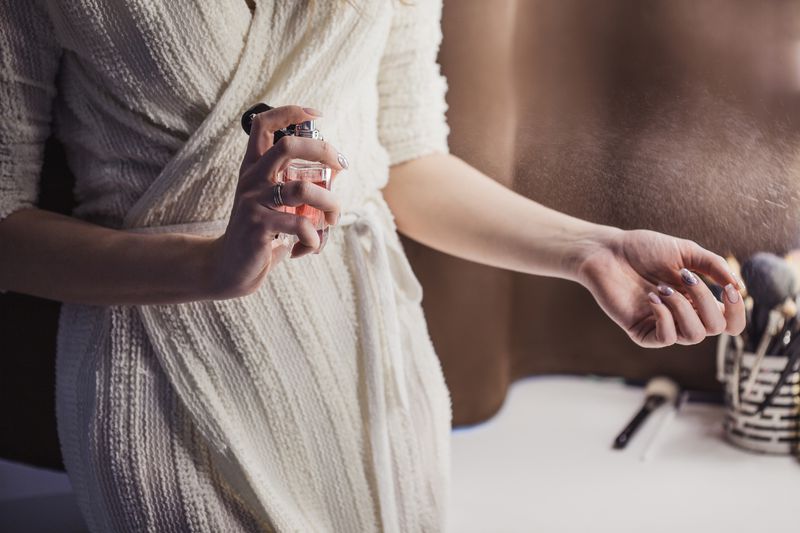 Young woman uses bottle of perfume at home, closeup