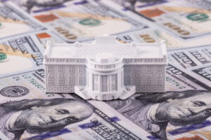 A miniature residence of the President of the United States, the White House, against the backdrop of 100 US dollar bills.