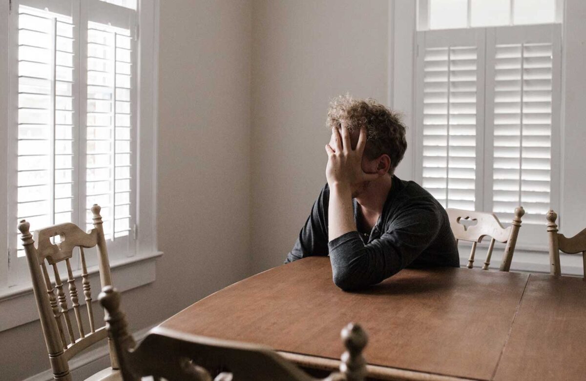 Man crying over money staring out the kitchen window.