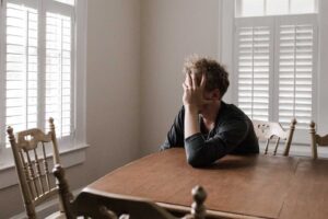 Man crying over money staring out the kitchen window.