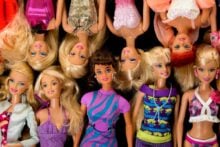 A group of Barbie dolls with various hairstyles, outfits, and accessories are arranged in two rows, some upright and some upside down, against a black background.