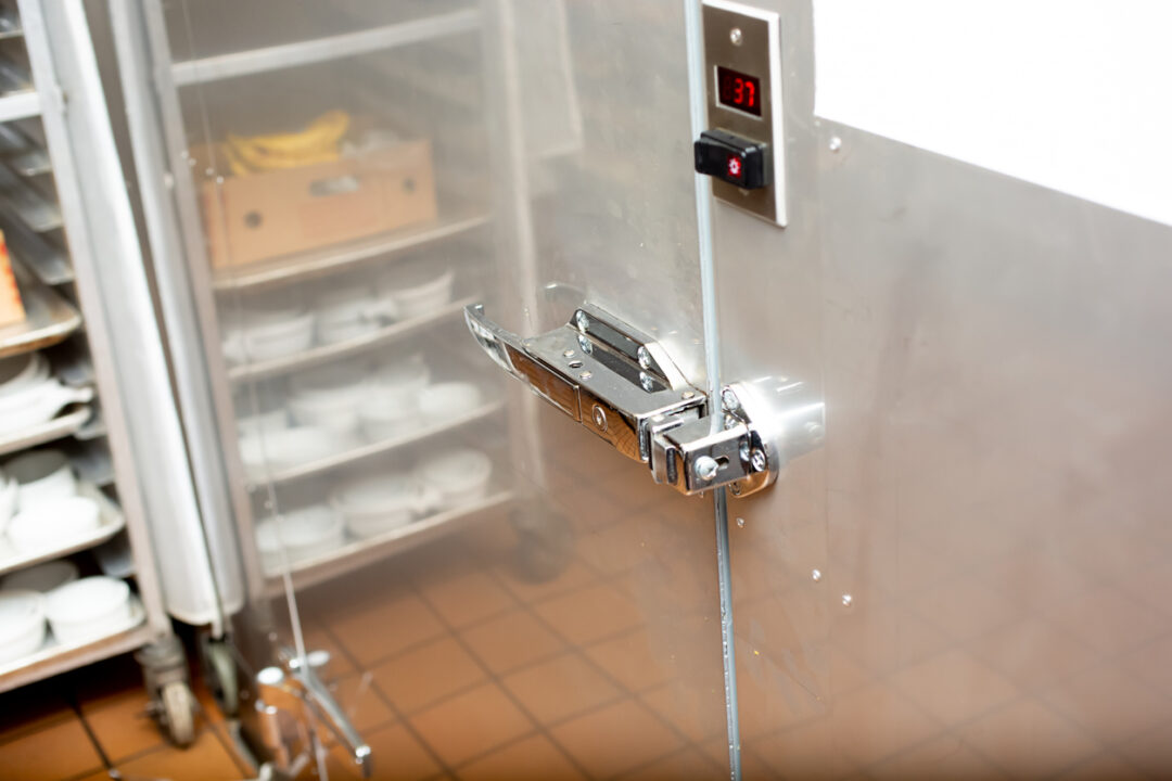 A view of a door handle that leads to a walk-in fridge inside a restaurant kitchen.