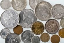 A close-up of assorted vintage U.S. coins, including silver dollars, half dollars, quarters, dimes, and various smaller denominations, with differing designs and dates visible.
