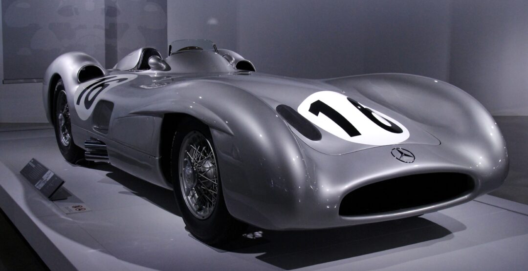 A sleek, silver vintage race car with the number 10 displayed prominently on its hood and sides. It features classic wire-spoke wheels and a low, aerodynamic body design.