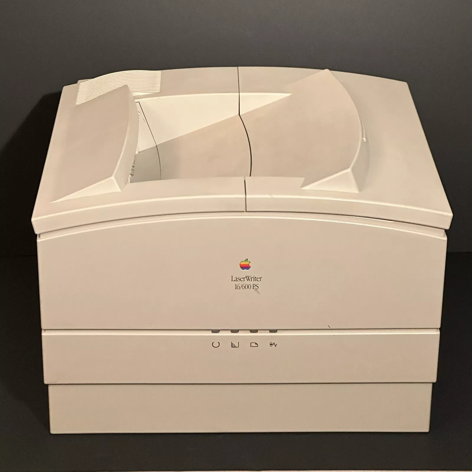 A vintage beige Apple LaserWriter 16/600 PS printer against a dark background. The printer has a paper tray on top and several buttons on the front panel.