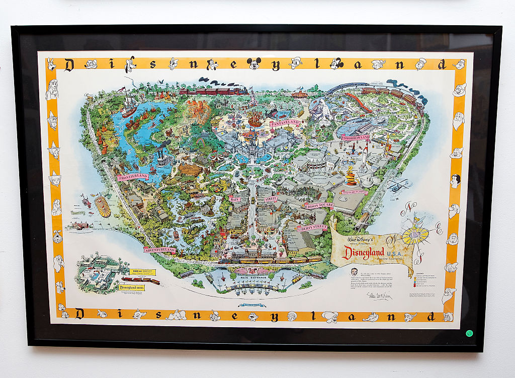 A framed vintage map of Disneyland U.S.A. is displayed. The map is colorful, showcasing various themed areas and attractions. It is surrounded by cartoon character illustrations along the border.