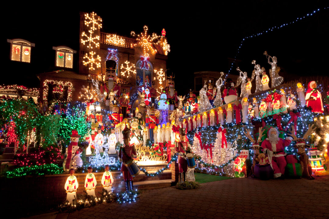 A house brightly decorated with an array of Christmas lights and inflatables. The display includes snowmen, nutcrackers, reindeer, Santas, and multicolored lights, creating a festive holiday scene.