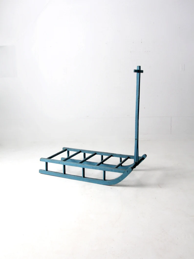 A minimalist, modern-style sled with a blue metal frame, featuring a rectangular base and a vertical handlebar against a plain white background.