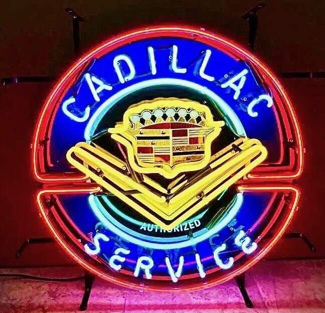 A neon sign displaying "Cadillac Service" with an emblem in the center, featuring bright red, blue, yellow, and white colors, illuminated against a dark background.