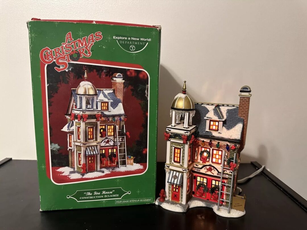 Model of a festive two-story house with holiday decorations, beside its box labeled "A Christmas Story." The house has snowy details, warm lights, and a small figure on the porch. The box features a similar house image and festive graphics.