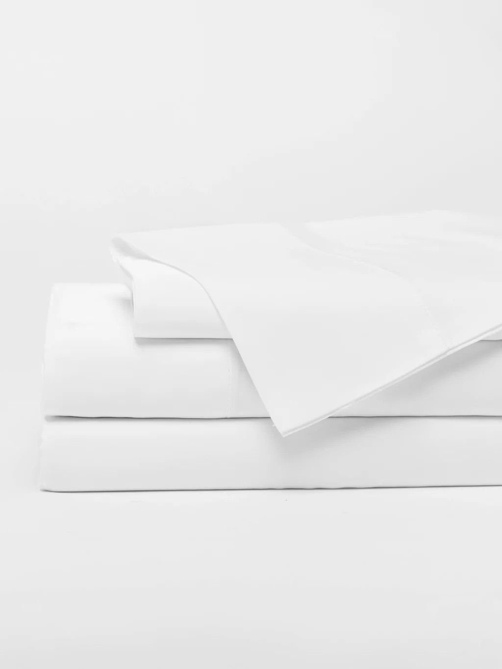 A neatly folded set of white bed sheets with pillowcases stacked on top, set against a plain white background.