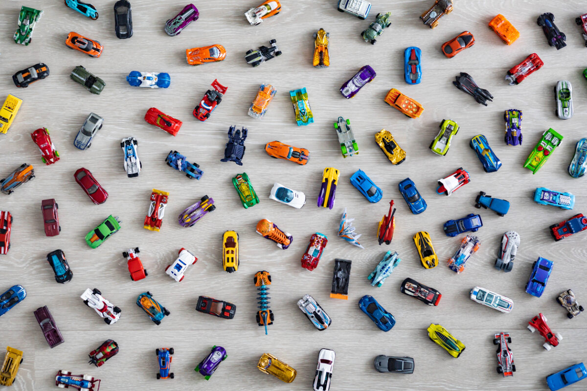 A collection of colorful Hot Wheels toy cars is arranged randomly on a light wooden surface. Various models and colors are visible, including blue, red, yellow, and more, creating a playful and vibrant pattern.