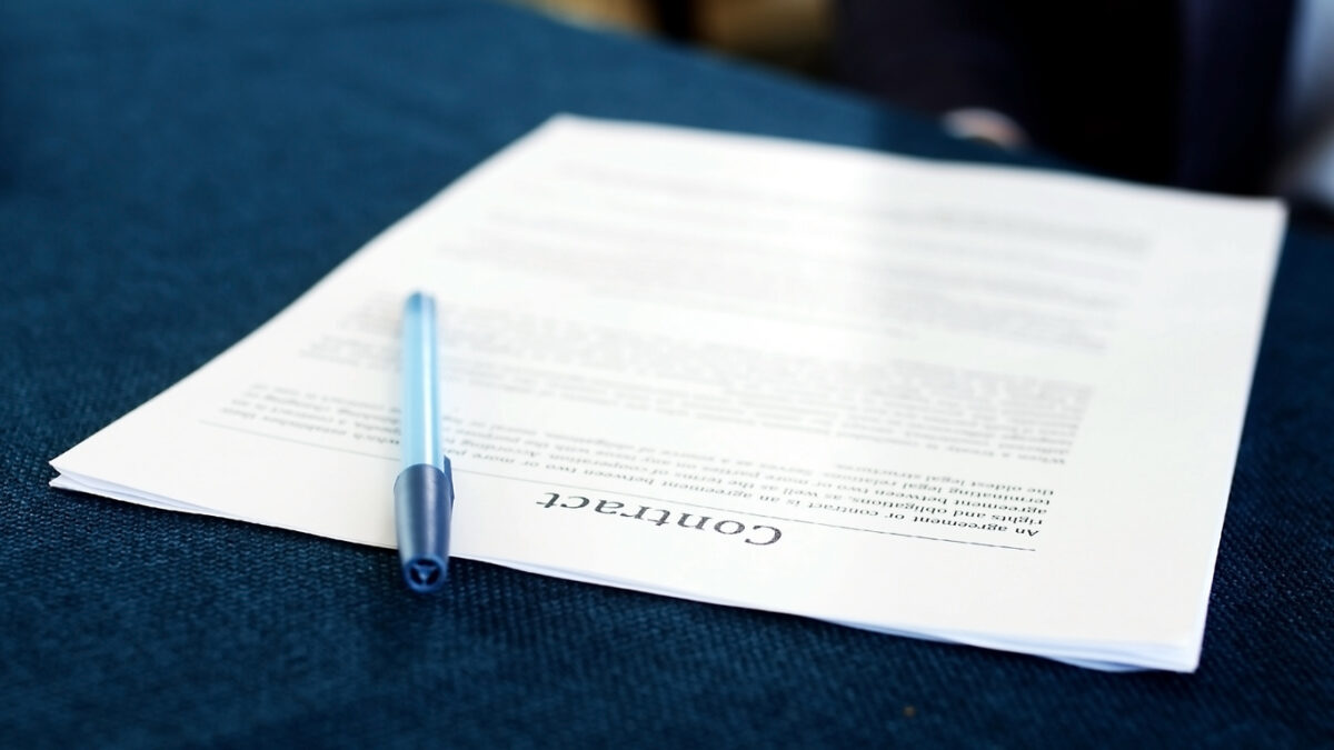 A pen rests on a partially readable contract nestled on a blue fabric surface. The document, slightly angled, prominently displays the word "contracts" at the bottom.