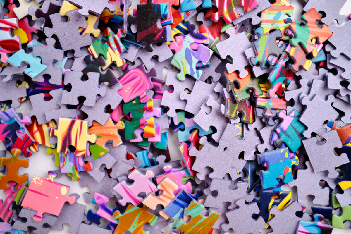 A scattered pile of colorful jigsaw puzzle pieces with various swirling patterns and hues, including blues, pinks, and oranges, against a bright background.