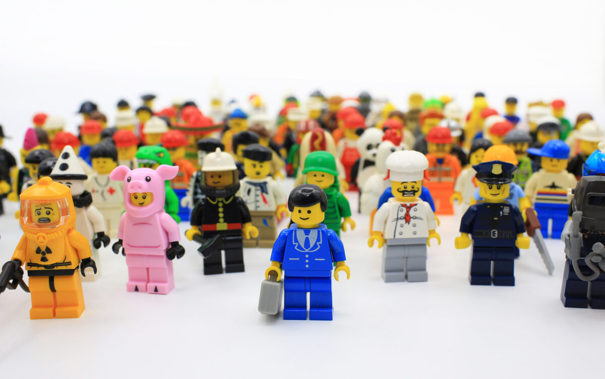 A diverse group of Lego minifigures in various costumes and uniforms, including a firefighter, pig suit, chef, and police officer, standing in rows against a plain background.