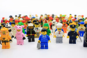 A diverse group of Lego minifigures in various costumes and uniforms, including a firefighter, pig suit, chef, and police officer, standing in rows against a plain background.