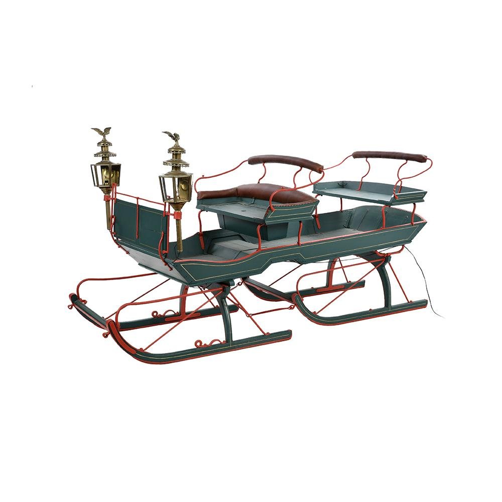 Image of a vintage green and red sleigh with two seats and ornate lanterns. The sleigh features elegant metal railings and detailed craftsmanship, giving it a classic and festive appearance.