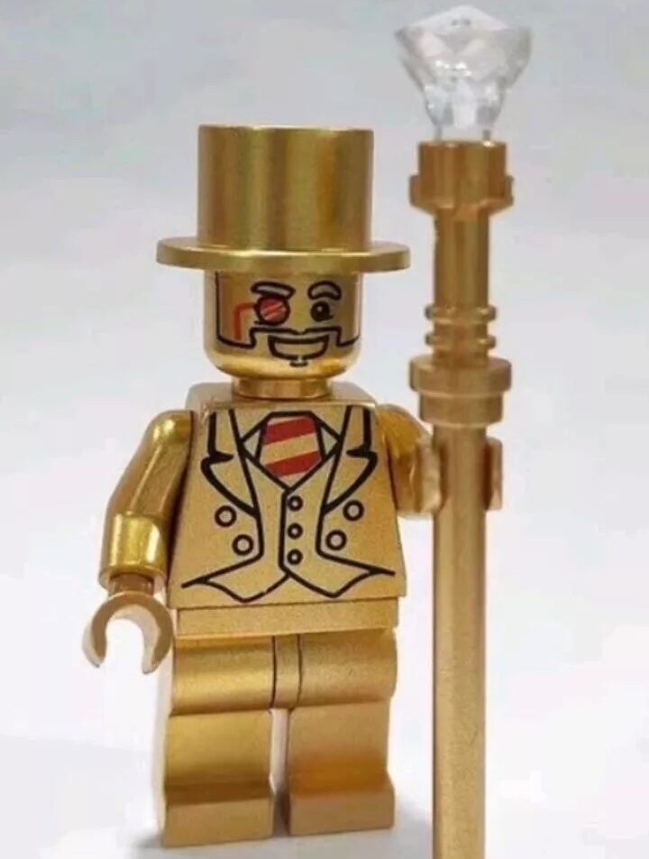 A golden LEGO figure wearing a top hat and monocle holds a staff with a crystal-like top. The figure is dressed in a suit with a striped shirt underneath, featuring a smiling face with a mustache.