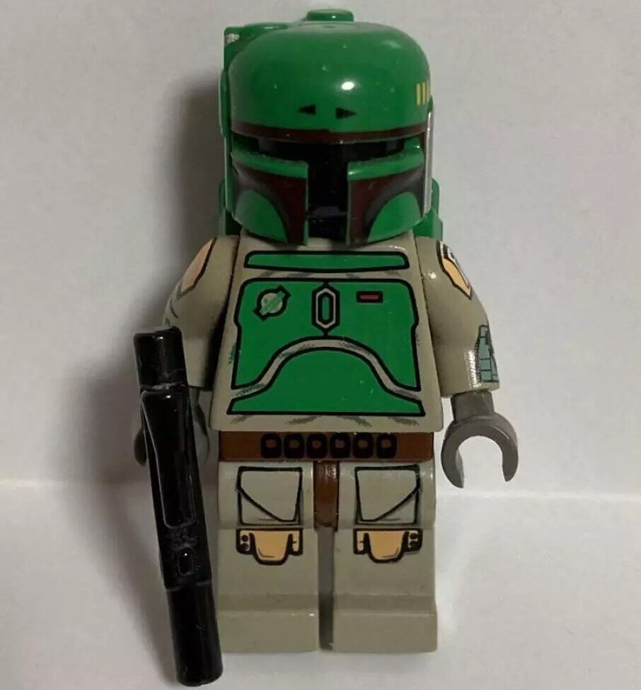 A LEGO minifigure resembling a character in green armor with a black visor and holding a black weapon, against a plain background.