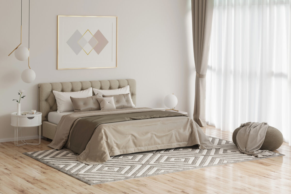 A modern bedroom with a neutral color palette features a tufted bed adorned with crisp beige sheets, a geometric patterned rug, white bedside table, pendant lights, and framed abstract artwork. Light floods in through sheer curtains on large windows.