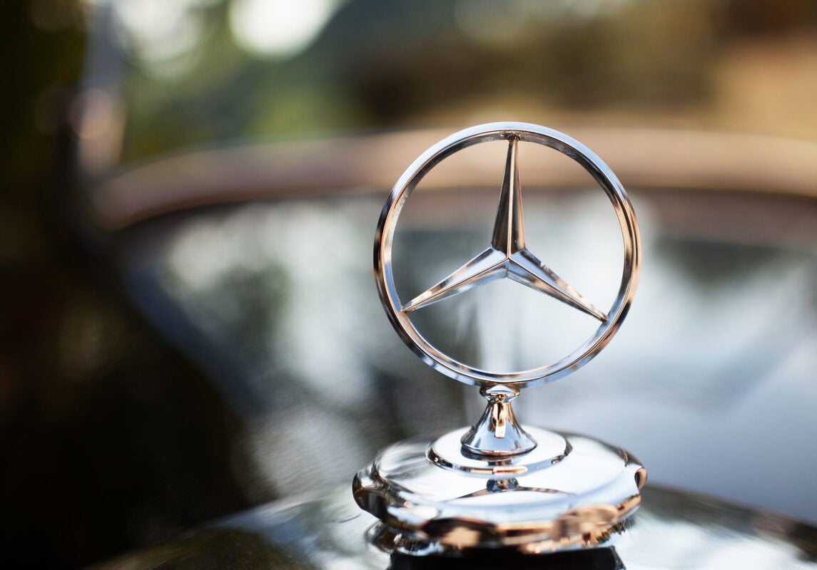 Close-up of a silver Mercedes-Benz hood ornament with a blurred background. The iconic three-pointed star emblem, often sought in high-end Mercedes-Benz auctions, is prominently displayed on the polished surface, suggesting luxury and elegance.