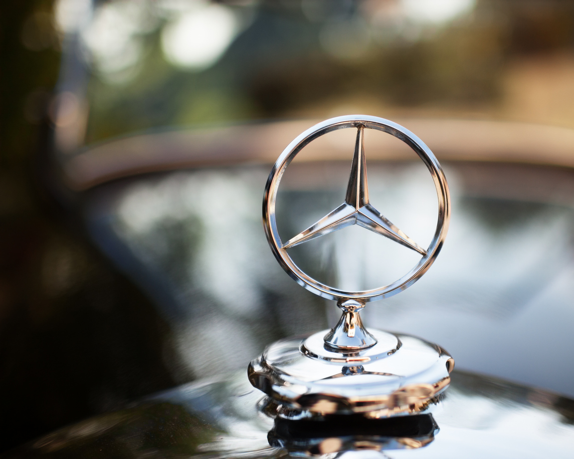 Close-up of a silver Mercedes-Benz hood ornament with a blurred background. The iconic three-pointed star emblem, often sought in high-end Mercedes-Benz auctions, is prominently displayed on the polished surface, suggesting luxury and elegance.