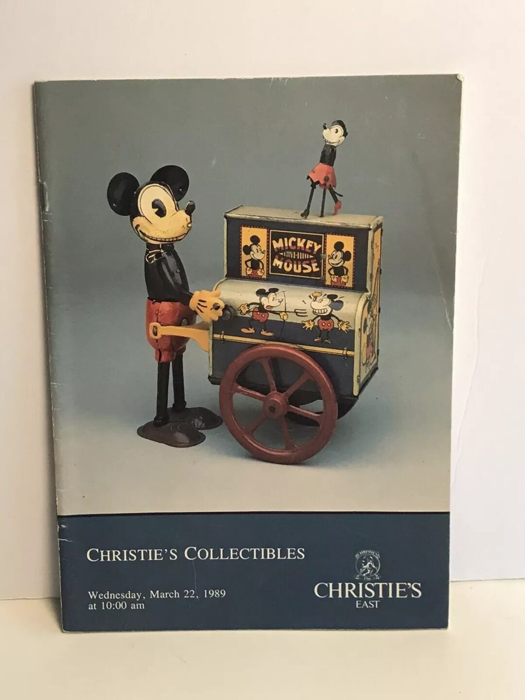 A vintage auction catalog cover featuring an old-fashioned Mickey Mouse figure with an organ grinder machine on wheels. The banner reads "Christie's Collectibles," with a date of Wednesday, March 22, 1989, at 10:00 am.