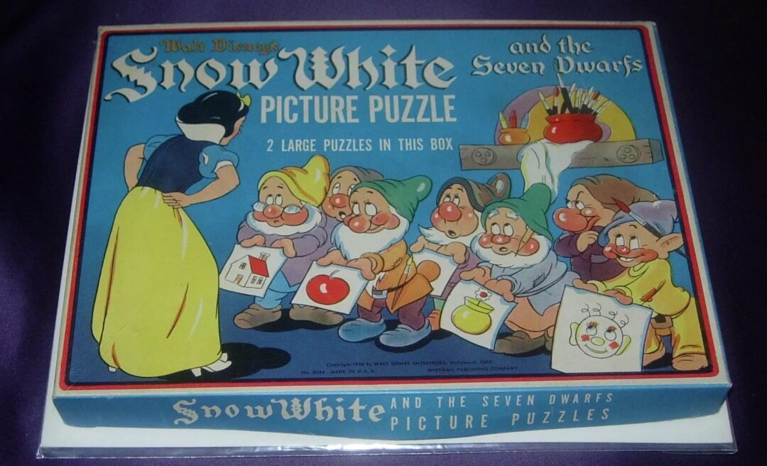 A vintage Disney puzzle box featuring an illustration of Snow White facing seven dwarfs. The dwarfs hold tools and a basket of apples. The text reads, "Snow White and the Seven Dwarfs Picture Puzzle - 2 Large Puzzles in This Box.