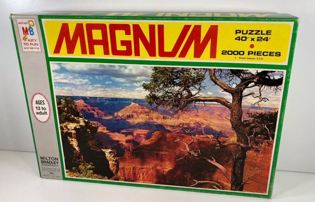 A sealed box of a 2000-piece Magnum puzzle featuring a scenic view of the Grand Canyon. The box is marked for ages 12 to adult and has dimensions of 40" x 24". It is branded with the Milton Bradley logo.